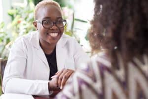 black woman doctor smiling holding mexican patient hand Mixed race young people at the doctors office