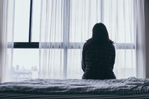 person sitting on bed looking out window considering high-functioning depression