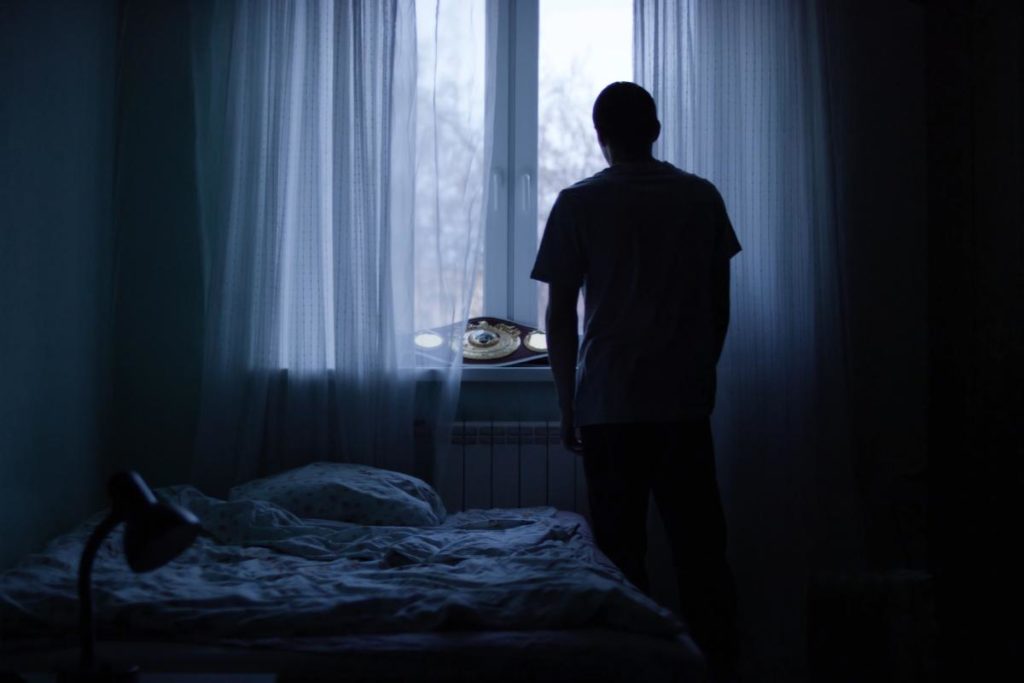 A person stands in a dark bedroom lit by a window learning about the side effects of opioids