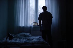 A person stands in a dark bedroom lit by a window learning about the side effects of opioids