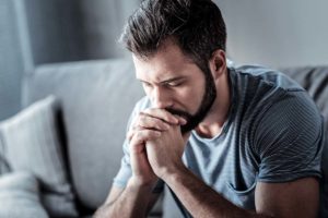 a person sits on a couch with their hands folded against their mouth while they learn of synthetic marijuana