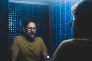 person stares at their reflection in a blue tiled bathroom while they deal with benzo abuse