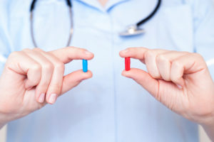 a doctor holds up a red pill and a blue pill to show color difference