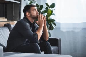 a person sits with their hands together on a couch as they experience the different types of anxiety