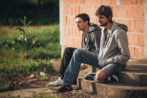two people sit outside on a curb while struggling with meth addiction
