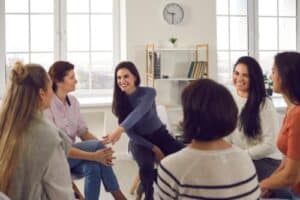 a woman leans over and touches the knee of another woman in her group therapy session while talking about the benefits of dialectical behavior therapy