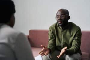 a man sits on a couch and talks to his therapist about issues during his ecstasy abuse rehab program