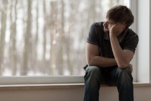 a person holds their head while sitting in a windowsill pondering how opioid addiction develops