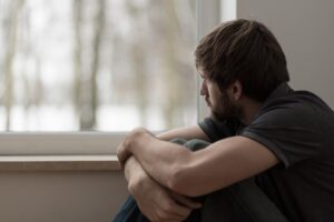 a man sits on the floor with his arms wrapped around his legs looking out a window wondering what is a depression disorder