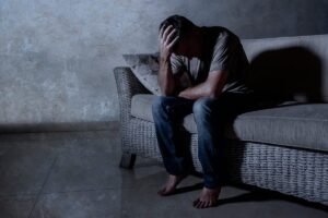 Man hangs head on couch in the dark, pondering the dangers of fentanyl addiction