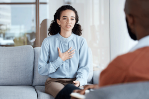 Woman grabs her chest while talking to therapist in anxiety treatment