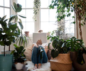 Woman sits and reads book about tips to combat depression, surrounded by plants
